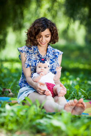 Young beautiful mother sits on blanket with her daughter during a picnic in the parkの写真素材