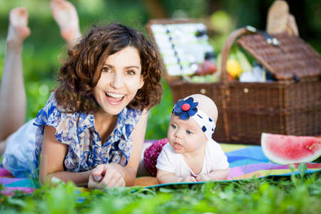 Young beautiful mother sits on blanket with her daughter during a picnic in the parkの写真素材