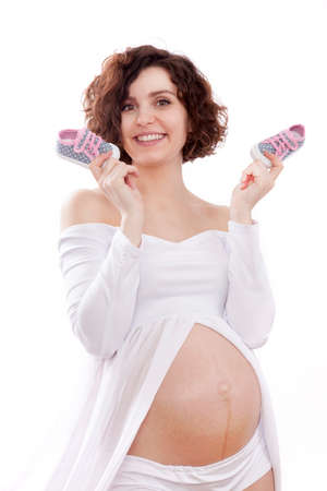 pregnant woman in a white dress holding a tiny baby shoes.の写真素材
