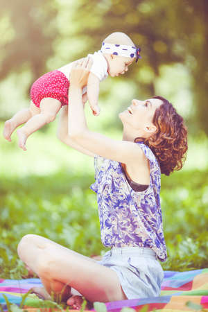 Young beautiful mother sits on blanket with her daughter during a picnic in the parkの写真素材
