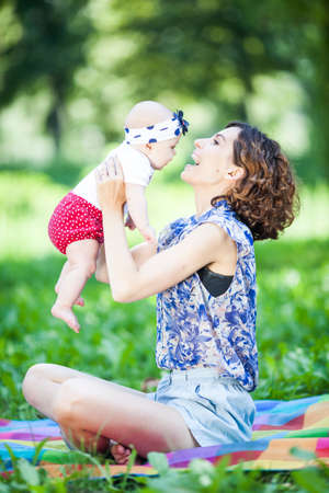 Young beautiful mother sits on blanket with her daughter during a picnic in the parkの写真素材
