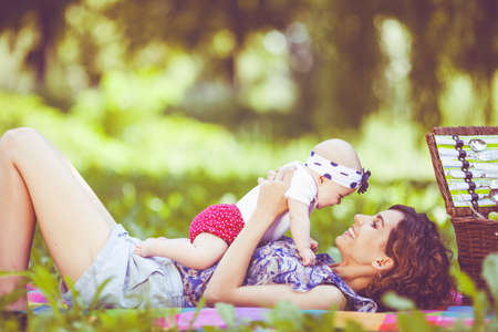 Young beautiful mother sits on blanket with her daughter during a picnic in the parkの写真素材