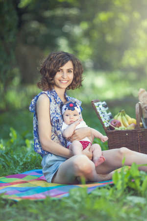 Young beautiful mother sits on blanket with her daughter during a picnic in the parkの写真素材
