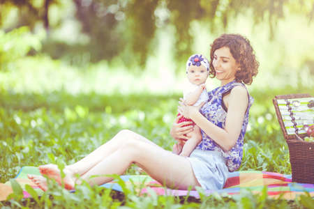 Young beautiful mother sits on blanket with her daughter during a picnic in the parkの写真素材
