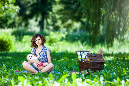 Young beautiful mother sits on blanket with her daughter during a picnic in the parkの写真素材