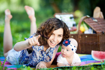 Young beautiful mother sits on blanket with her daughter during a picnic in the parkの写真素材