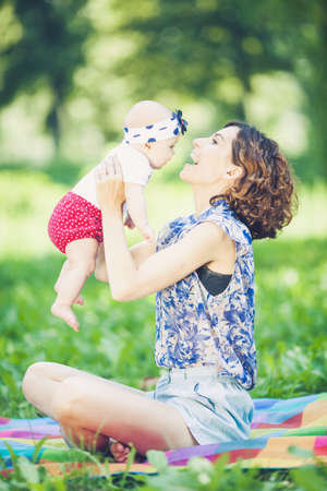 Young beautiful mother sits on blanket with her daughter during a picnic in the parkの写真素材