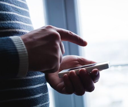 The man is using a smartphone. Modern mobile phone in hand.