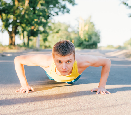 Closeup portrait, young healthy handsome man performing pushup outside on road in park