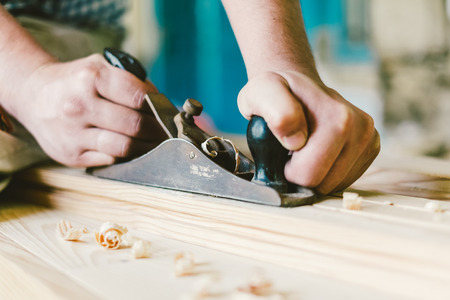 Man hands with carpenters plane on wooden backgroundの写真素材