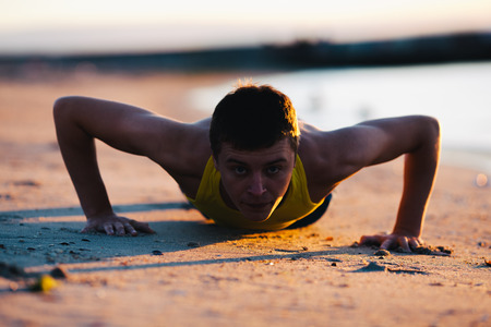 Young man doing push ups on a beach