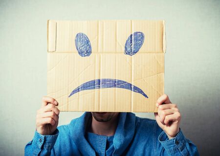 Curly man with a kraft cardboard instead of a head, a sad smiley. On a gray background.の写真素材