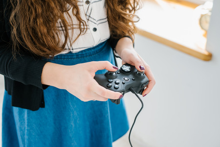 Attractive young woman with long curly brunette hair on a background window playing computer game at...