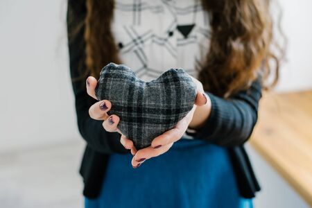Picture of a small gray heart in hands, female holds handmade sewn soft toy, woman with Valentine gift against the window, happy girl smiling, conceptual image of health care or love.の写真素材