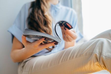 Attractive girl reading magazine on  window. girl holding magazine at homeの写真素材
