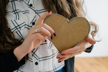 A young woman holds out a cut out construction paper heart near the window.