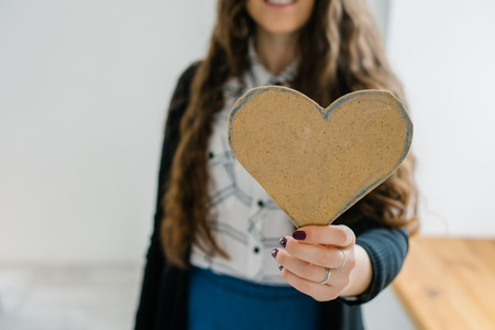 A young woman holds out a cut out construction paper heart near the window.の写真素材