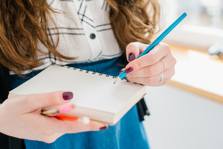 Close-up of a female hand writing on an blank notebook with a blue pen.の写真素材
