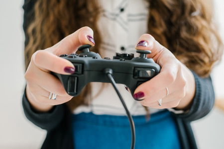 Attractive young woman with long curly brunette hair on a background window playing computer game at home.の写真素材
