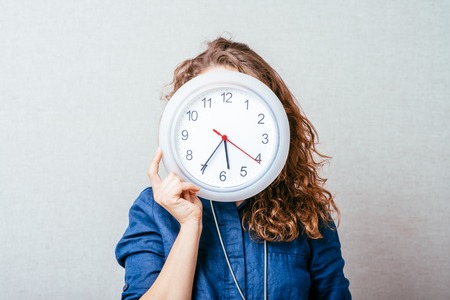Curly girl with a wall clock. Gray background.