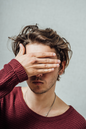 young man closes his eyes with his handsの写真素材