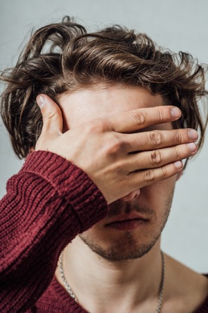 young man closes his eyes with his handsの写真素材