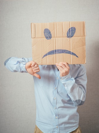 Young man with an unhappy smiley card half covering faceの写真素材