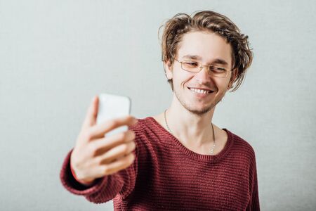 Cheerful selfie. Cheerful young man  making photo of himself while standing against grey backgroundの写真素材