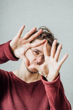 A man looking through his hands in the shape of a heart. On a gray background.の写真素材