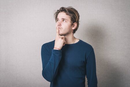 Man thinks finger to his mouth. Gray background