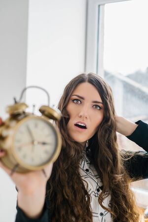 Closeup portrait woman extending hand to alarm clock. Human face expression, emotion, feeling.