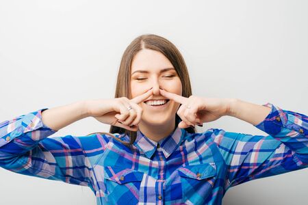 Beautiful young lady covers nose with hand showing that something stinks, isolated on whiteの写真素材