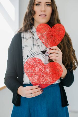 Beautiful with long curly brunette hair girl with two hearts against the window.
