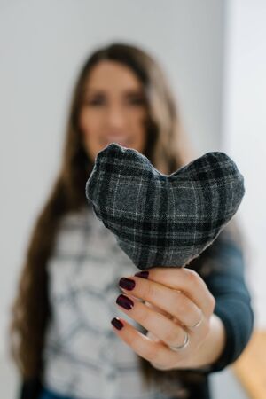 Picture of a small gray heart in hands, female holds handmade sewn soft toy, woman with Valentine gift against the window, happy girl smiling, conceptual image of health care or love.の写真素材