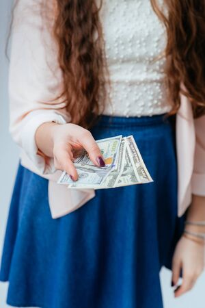 long-haired beautiful young brunette woman in blue long dress holds money in hands, received salary and considersの写真素材