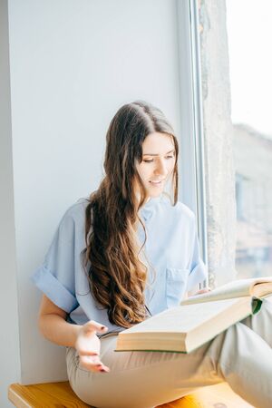 Young girl reading book by the window