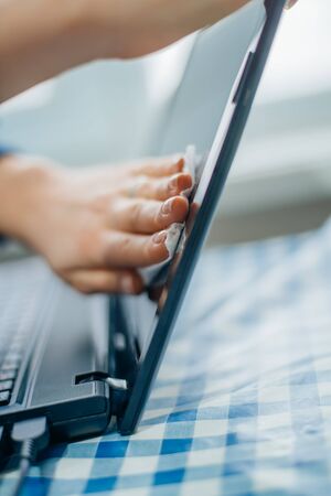 people, housework, electronics and housekeeping concept - close up of woman hand cleaning laptop computer screen with clothの写真素材