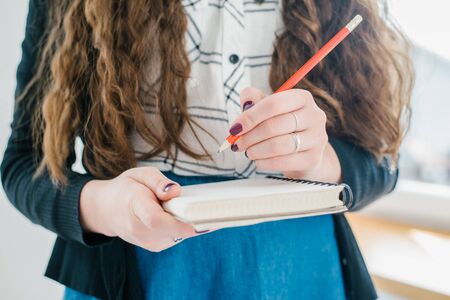 young caucasian brunette haired happy smiling business woman holding diary and red pancilの写真素材