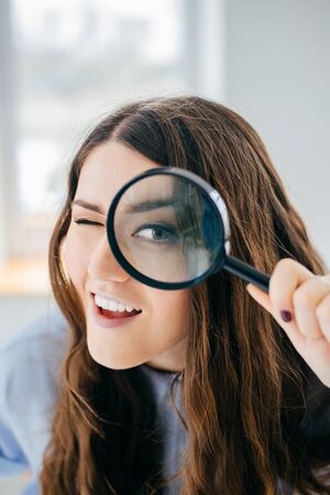 Young beautiful woman with magnifying glass near the window.の写真素材