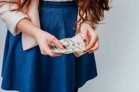 long-haired beautiful young brunette woman in blue long dress holds money in hands, received salary and considersの写真素材