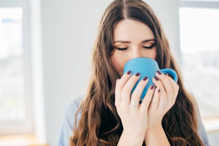 Portrait of a young woman near the window with cup of teaの写真素材