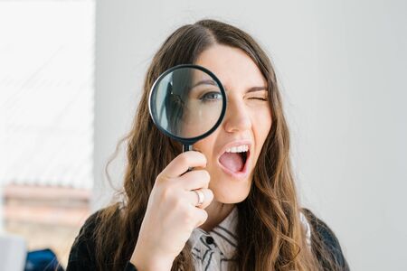 on a gray background young girl looking through a magnifying glassの写真素材