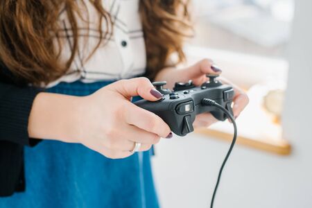 Attractive young woman with long curly brunette hair on a background window playing computer game at...