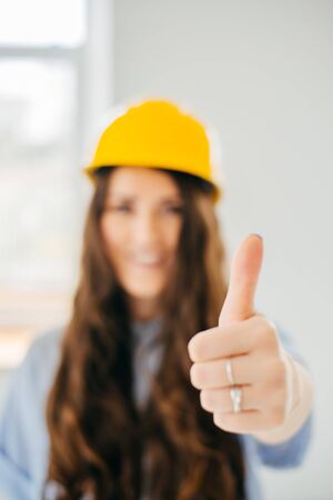 woman in yellow helmet young engineer showing okay sign against the window