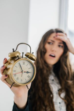 Closeup portrait woman extending hand to alarm clock. Human face expression, emotion, feeling.の写真素材