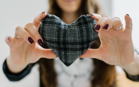 Picture of a small gray heart in hands, female holds handmade sewn soft toy, woman with Valentine gift against the window, happy girl smiling, conceptual image of health care or love.の写真素材