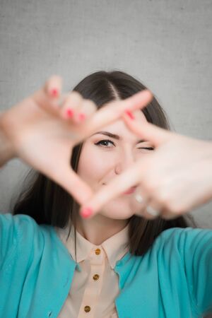 Gesturing finger frame. Beautiful young woman looking at camera and gesturing finger frame while standing against grey backgroundの写真素材