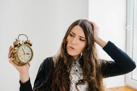 Closeup portrait woman extending hand to alarm clock. Human face expression, emotion, feeling.の写真素材