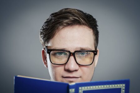 Portrait of young man in glasses reading isolated over grey backgroundの写真素材