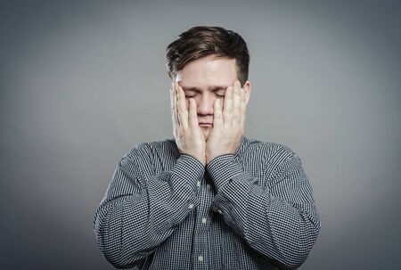 a young man upset with hands on faceの写真素材